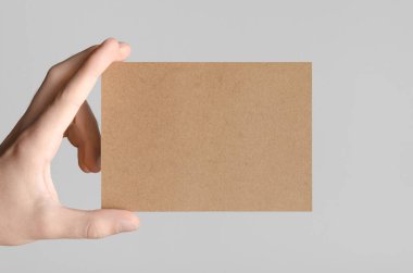 Kraft A6 el ilanı / kart / davet Mock-Up - kraft el ilanı gri bir arka plan üzerinde tutan eller erkek.