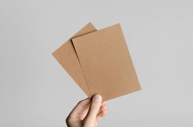 Kraft A6 el ilanı / kart / davet Mock-Up-kraft el ilanları gri bir arka plan üzerinde holding erkek eller.