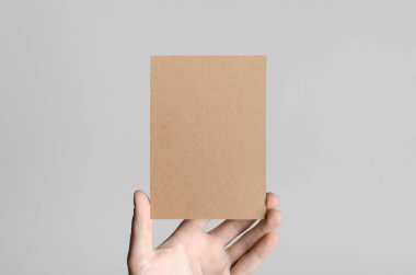 Kraft A6 el ilanı / kart / davet Mock-Up - kraft el ilanı gri bir arka plan üzerinde tutan eller erkek.