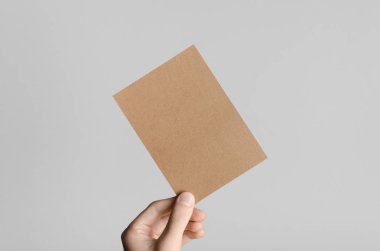 Kraft A6 el ilanı / kart / davet Mock-Up - kraft el ilanı gri bir arka plan üzerinde tutan eller erkek.