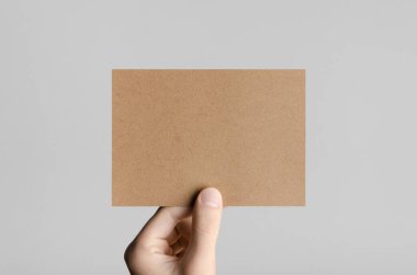 Kraft A6 el ilanı / kart / davet Mock-Up - kraft el ilanı gri bir arka plan üzerinde tutan eller erkek.