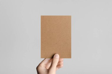 Kraft A6 el ilanı / kart / davet Mock-Up - kraft el ilanı gri bir arka plan üzerinde tutan eller erkek.