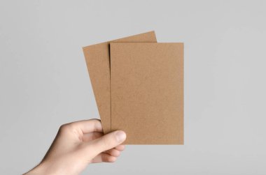 Kraft A6 el ilanı / kart / davet Mock-Up-kraft el ilanları gri bir arka plan üzerinde holding erkek eller.