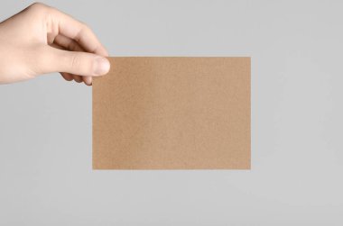Kraft A6 el ilanı / kart / davet Mock-Up - kraft el ilanı gri bir arka plan üzerinde tutan eller erkek.