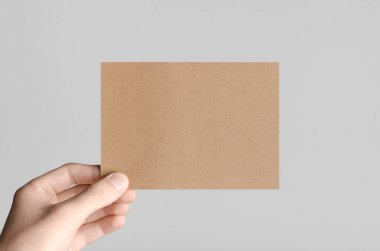 Kraft A6 el ilanı / kart / davet Mock-Up - kraft el ilanı gri bir arka plan üzerinde tutan eller erkek.