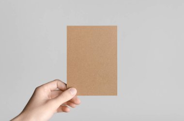 Kraft A6 el ilanı / kart / davet Mock-Up - kraft el ilanı gri bir arka plan üzerinde tutan eller erkek.