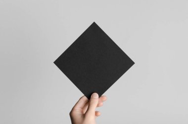 Siyah kare el ilanı / davet Mock-Up - erkek eller gri bir arka plan üzerinde siyah bir el ilanı holding.
