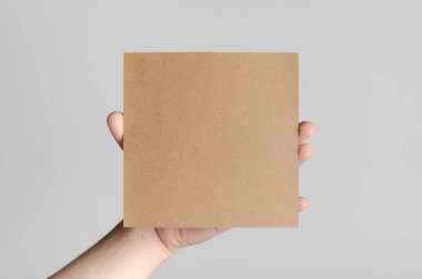 Kraft kare el ilanı / davet Mock-Up - kraft el ilanı gri bir arka plan üzerinde tutan eller erkek.