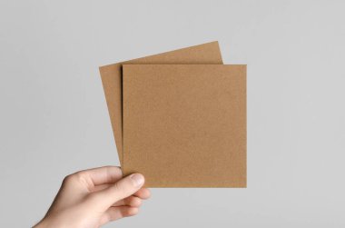 Kraft kare el ilanı / davet Mock-Up-kraft el ilanları gri bir arka plan üzerinde holding erkek eller.