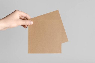 Kraft kare el ilanı / davet Mock-Up-kraft el ilanları gri bir arka plan üzerinde holding erkek eller.