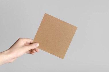 Kraft kare el ilanı / davet Mock-Up - kraft el ilanı gri bir arka plan üzerinde tutan eller erkek.