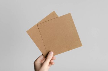 Kraft kare el ilanı / davet Mock-Up-kraft el ilanları gri bir arka plan üzerinde holding erkek eller.