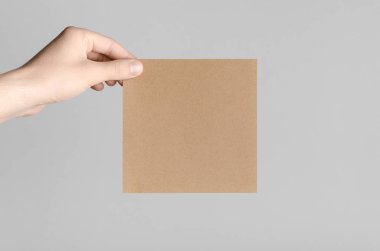 Kraft kare el ilanı / davet Mock-Up - kraft el ilanı gri bir arka plan üzerinde tutan eller erkek.