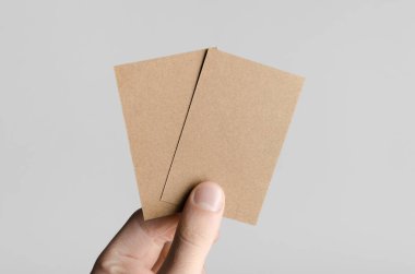 Kraft kartvizit Mock-Up (85x55mm) - kraft kartları gri bir arka plan üzerinde holding erkek eller.