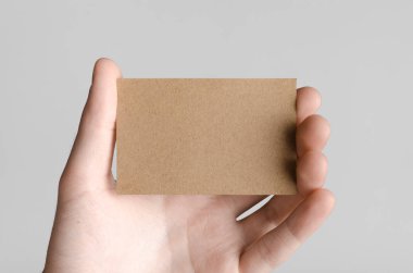 Kraft kartvizit Mock-Up (85x55mm) - kraft kartı gri bir arka plan üzerinde holding erkek eller.