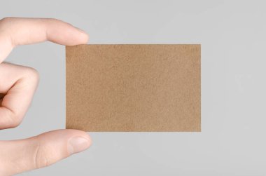 Kraft kartvizit Mock-Up (85x55mm) - kraft kartı gri bir arka plan üzerinde holding erkek eller.