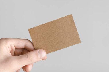 Kraft kartvizit Mock-Up (85x55mm) - kraft kartı gri bir arka plan üzerinde holding erkek eller.