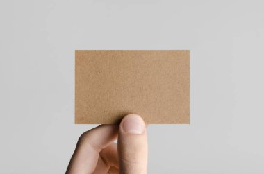 Kraft kartvizit Mock-Up (85x55mm) - kraft kartı gri bir arka plan üzerinde holding erkek eller.