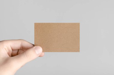 Kraft kartvizit Mock-Up (85x55mm) - kraft kartı gri bir arka plan üzerinde holding erkek eller.