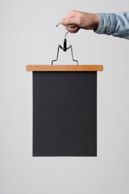 Siyah A4 Afiş / Poster Mock-Up-elbise askısı üzerinde beyaz bir arka plan üzerinde siyah bir poster tutan adam.