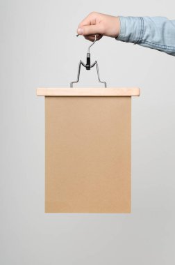 Kraft A4 Afiş / Poster Mock-Up-kraft poster beyaz bir arka plan üzerinde elbise askısı üzerinde tutan adam.