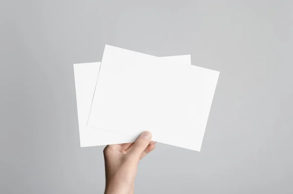 A5 Flyer / Invitation Mock-Up - Male hands holding blank flyers on a gray background.