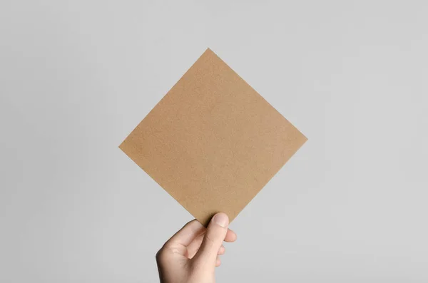 Kraft Square Flyer / Invitation Mock-Up - Male hands holding a kraft flyer on a gray background.