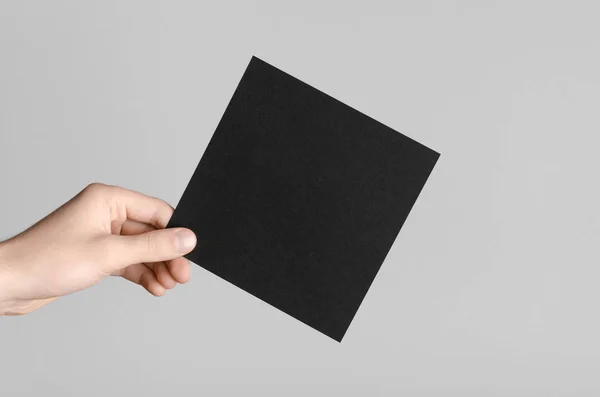 Black Square Flyer / Invitation Mock-Up - Male hands holding a black flyer on a gray background.
