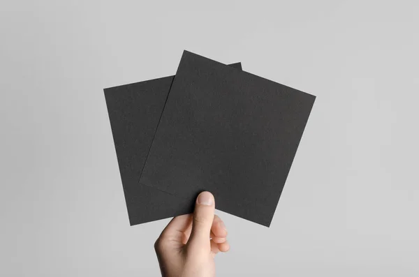 Black Square Flyer / Invitation Mock-Up - Male hands holding black flyers on a gray background.