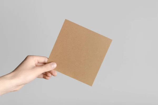 Kraft Square Flyer / Invitation Mock-Up - Male hands holding a kraft flyer on a gray background.