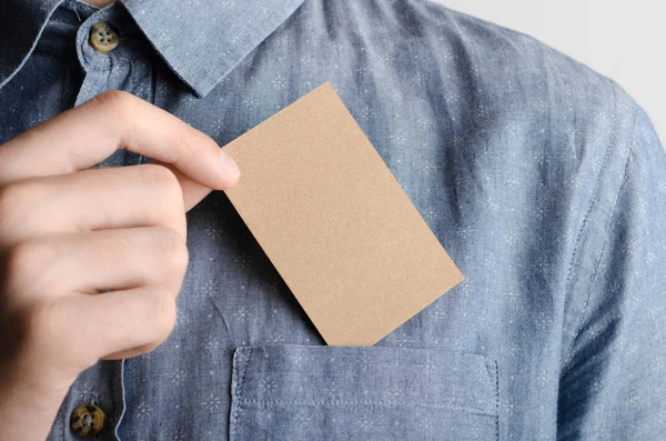 Kraft Business Card Mock-Up (85x55mm) - Man in a chambray shirt holding a kraft card on a gray background.