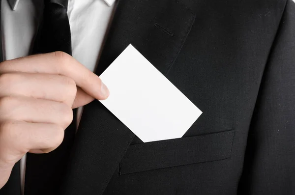 Business Card Mock-Up (85x55mm) - Man in a black suit holding a blank card on a gray background.