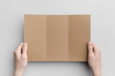 Kraft A4 üç katlı broşür Mock-Up - erkek kraft üç katlı bir gri arka plan üzerinde tutan eller.