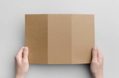 Kraft A4 üç katlı broşür Mock-Up - erkek kraft üç katlı bir gri arka plan üzerinde tutan eller.