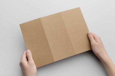 Kraft A4 üç katlı broşür Mock-Up - erkek kraft üç katlı bir gri arka plan üzerinde tutan eller.