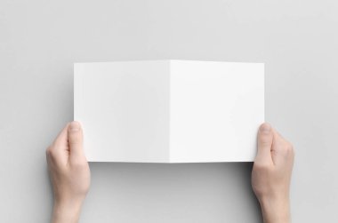 İkiye katlanmış broşür Mock-Up - erkek elleri boş bir ikiye katlanmış bir gri arka plan üzerinde tutarak kare.