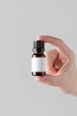 Damlalık şişe Mock-Up. Boş etiket - erkek bir damlalık şişe gri bir arka plan üzerinde tutan eller