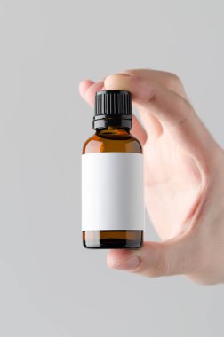 Damlalık şişe Mock-Up. Boş etiket - erkek bir damlalık şişe gri bir arka plan üzerinde tutan eller