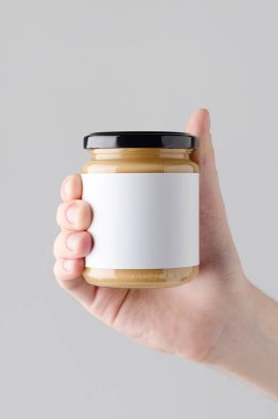 Fıstık / badem / fındık ezmesi kavanozu Mock-Up. Boş etiket - gri bir arka plan üzerinde bir fındık ezmesi kavanoz holding erkek eller