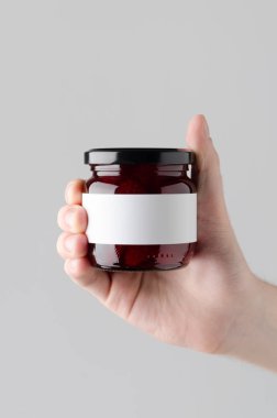 Çilek reçeli kavanoz Mock-Up. Boş etiket - gri bir arka plan üzerinde bir reçel kavanoz holding erkek eller
