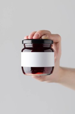 Kiraz reçel kavanoz Mock-Up. Boş etiket - gri bir arka plan üzerinde bir reçel kavanoz holding erkek eller