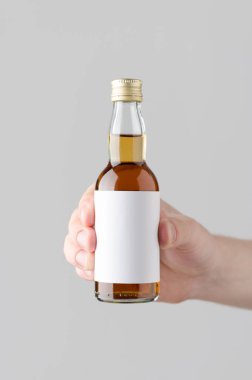 Minyatür ruhları / içki şişesi Mock-Up. Boş etiket - gri bir arka plan üzerinde bir içki şişesi holding erkek eller