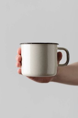 Beyaz emaye kupa Mock-Up - erkek bir emaye kupa gri bir arka plan üzerinde tutan eller