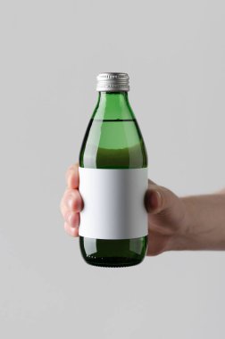 Su şişesi Mock-Up. Boş etiket - erkek gri bir arka plan üzerinde bir su şişesi tutan eller