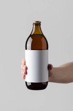 Bira şişe Mock-Up. Boş etiket - gri bir arka plan üzerinde bir bira şişesi holding erkek eller