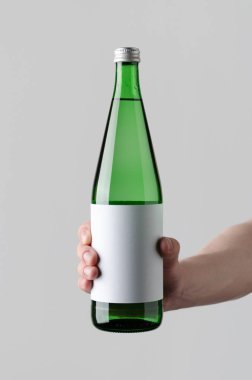 Su şişesi Mock-Up. Boş etiket - erkek gri bir arka plan üzerinde bir su şişesi tutan eller