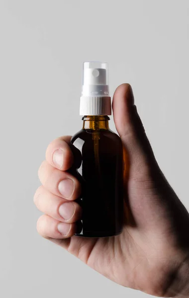 Amber Spray Bottle Mock-Up - Male hands holding an amber spray bottle on a gray background