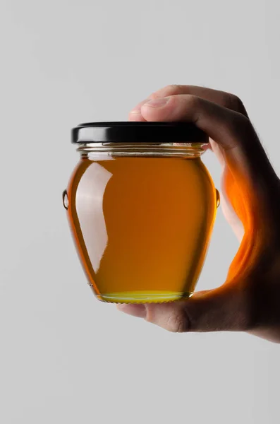 蜂蜜瓶モックアップ 灰色の背景に蜂蜜の瓶を保持している男性の手 — ストック写真