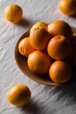 Portakal beyaz keten masa örtüsü üzerinde ahşap bir kasede.