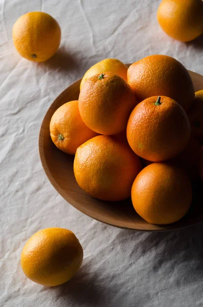 Portakal beyaz keten masa örtüsü üzerinde ahşap bir kasede.
